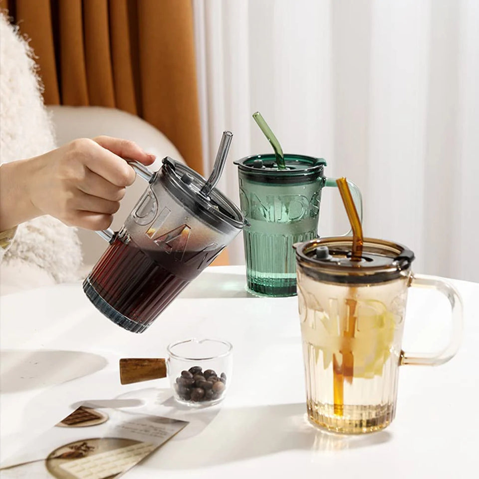 Person holding a glass with a straw, surrounded by various drinks on a table.