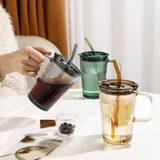 Person holding a glass with a straw, surrounded by various drinks on a table.