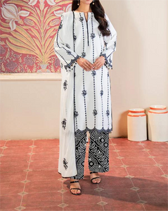 Woman wearing a white and black patterned outfit with a scarf in a room with decorative wall and floor.