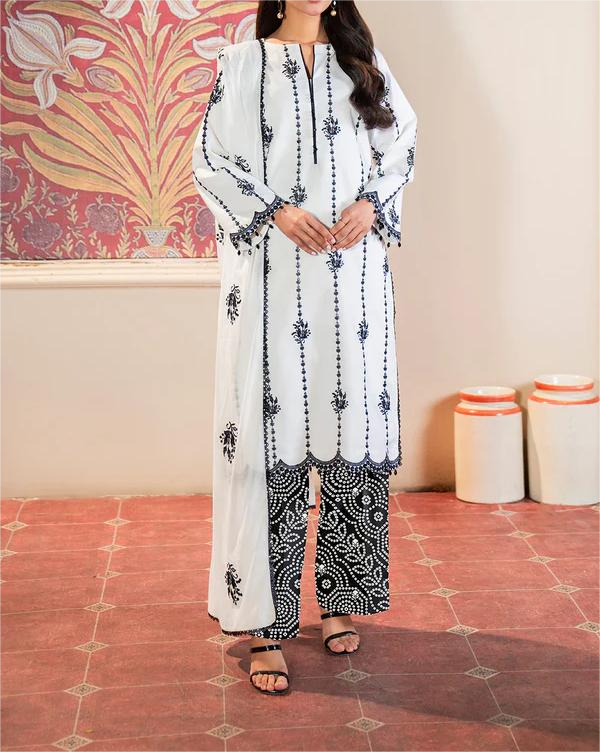 Woman wearing a white and black patterned outfit with a scarf in a room with decorative wall and floor.