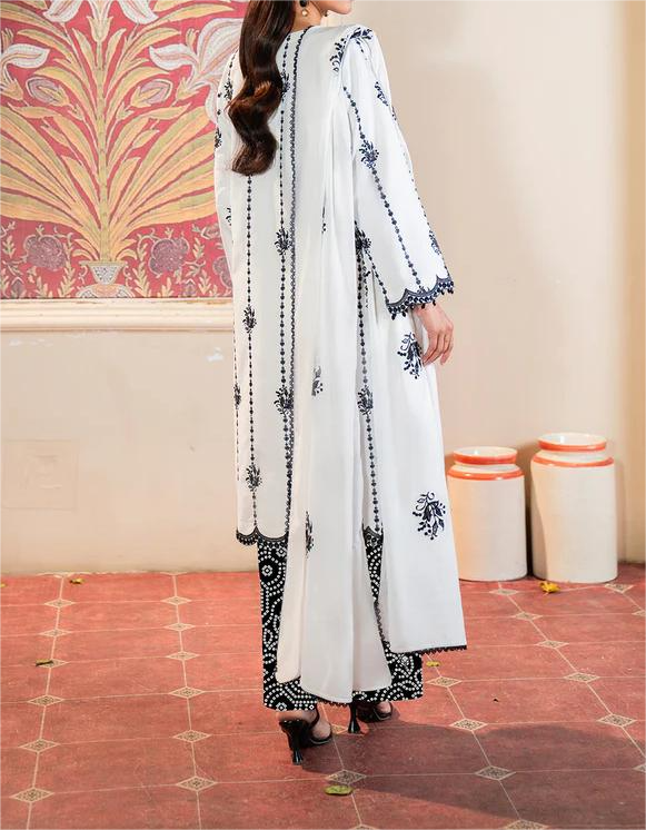 Woman wearing a white and black embroidered outfit in a room with decorative wall and floor.
