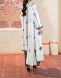 Woman wearing a white and black embroidered outfit in a room with decorative wall and floor.
