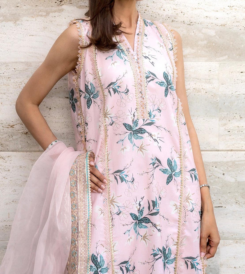 Woman wearing a light pink floral dress with a matching dupatta against a textured white wall.