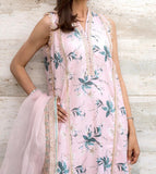 Woman wearing a light pink floral dress with a matching dupatta against a textured white wall.